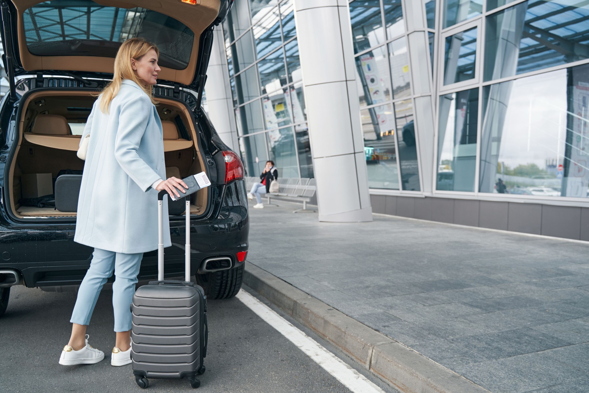 Passenger with travel document and baggage near open car trunk